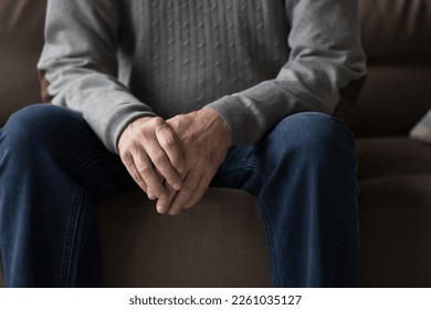 Senior older man in casual clothes sitting on home sofa, holding hands, folding palms, leaning elbows on hips, keeping pose for conversation, body gesture of waiting, anxiety. Close up of male hands - Powered by Shutterstock