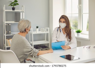 Senior Patient And Female Doctor Wearing Protective Masks At Clinic. Mature Woman Visiting Physician To Treat Virus At Hospital