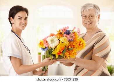 Senior Patient Giving Flowers To Nurse. Looking At Camera, Smiling.?