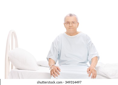 Senior patient in a hospital gown sitting on a bed and looking at the camera isolated on white background - Powered by Shutterstock