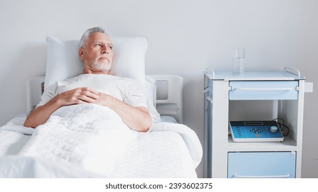 Senior patient rests while lying on the bed, recovering in modern hospital ward. Hospitalization. Treatment and healing. Coronavirus and pandemic concept - Powered by Shutterstock