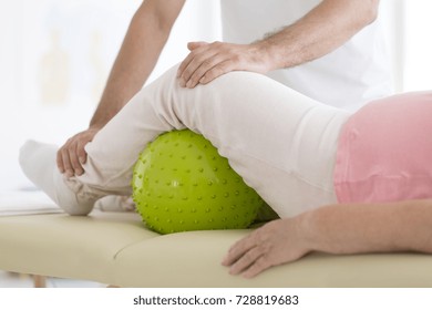 Senior patient undergoing rehabilitation in a hospital with a green massage ball under her left leg - Powered by Shutterstock