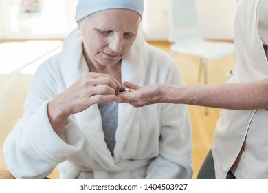 Senior Patient Wearing Bathrobe And Headscarf At Hospice Taking Pills From Her Nurse
