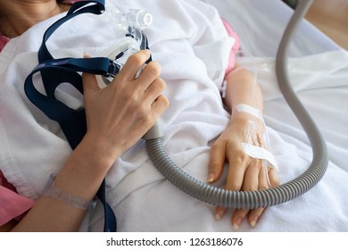 Senior Patient Woman Hand Holding Cpap Mask Between The Chest Lying  In Hospital Room.
Obstructive Sleep Apnea Therapy.