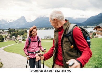 Senior Pensioner Couple With Nordic Walking Poles Hiking In Nature, Talking.