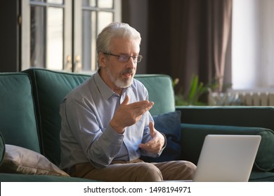 Senior Pensioner Man Sit On Couch In Living Room Talk On Video Call On Laptop, Mature Grandfather Use Wireless Fast Internet Connection, Speak With Family On Computer, Elderly And Technologies Concept