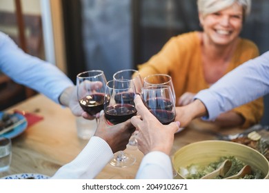 Senior people having fun cheering with wine at patio dinner - Focus on female face - Powered by Shutterstock