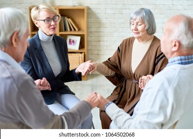 Senior People Holding Hands In Group Therapy Session Lead By Female Psychiatrist, Focus On Elegant Elderly Woman With Eyes Closed, Copy Space