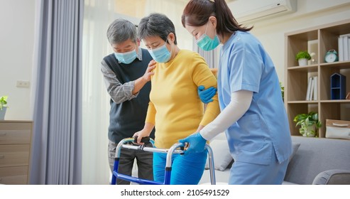 Senior People Home Healthcare Concept - Asian Female Doctor Wearing Face Mask Is Teaching Residential Rehabilitation With Walker Frame To Senior Woman While Elder Man Take Care Of Her