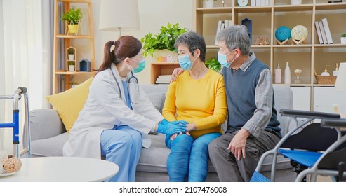 Senior People Home Healthcare Concept - Asian Female Doctor Wearing Face Mask Is Talking To Senior Woman While Elder Man Take Care Of Her