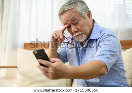 Senior people lifestyle health problem concept : Portrait photo of senior Asian man has a eye long sighted problem trying to read message from smartphone.