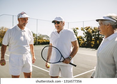 Senior people playing tennis on a sunny day. Cheerful old men standing on tennis court holding racket and balls. - Powered by Shutterstock