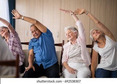 Senior people stretching while sitting on chairs at retirement home - Powered by Shutterstock