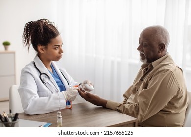 Senior People Support Concept. Portrait Of Black Medical Worker Holding Personal Alarm Button And Giving It To Mature Patient, Sitting At Table In Office, Explaining How To Use Medical Alert