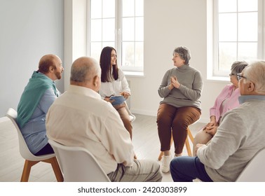 Senior people talking at group therapy meeting. Old male and female patients at nursing home discussing aging issues at training workshop seminar with young smiling therapist coach girl with clipboard - Powered by Shutterstock