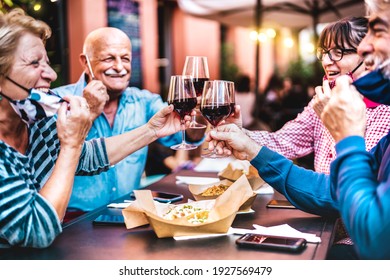 Senior people toasting wine at restaurant bar wearing open face masks - New normal life style concept with happy mature friends having fun together at garden party - Vivid filter with focus on glasses
