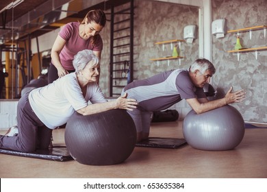 Senior people workout in rehabilitation center. Personal trainer helping senior people on Pilates ball.
