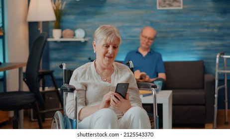 Senior person sitting in wheelchair and using smartphone to browse internet and discover technology. Elder woman suffering from chronic disability and looking at mobile phone screen. - Powered by Shutterstock