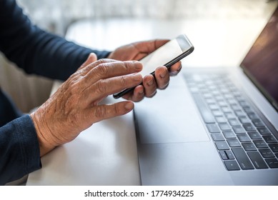 Senior person using mobile phone and laptop at home. Closeup of the wrinkled hands. Blank screen. 