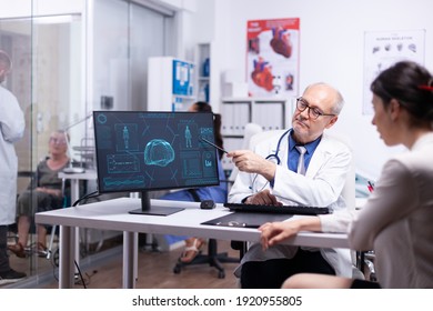 Senior physician showing scan body result to young patient pointing with pancil on desktop. Doctor and woman discussing in front of pc about brain functions, medical consultation in hospital clinic