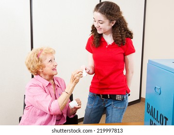 Senior Poll Worker Hands A Sticker To A Young First Time Voter.  