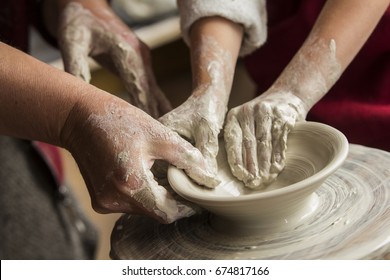 Senior Potter Teaching A Little Girl The Art Of Pottery. Child Working With Clay Creating Ceramic Pot On Sculpting Wheel