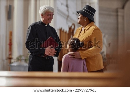 Senior priest discussing ceremony together with woman and her granddaughter while they visiting the old church