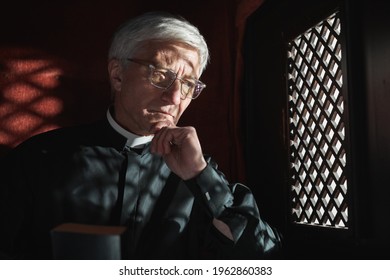 Senior priest sitting behind the grid and listening the confession in the church