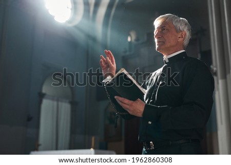 Senior priest standing with the Bible during ceremony in the church