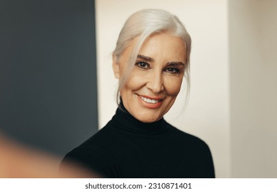 Senior professional woman with silver hair flashing a warm and genuine smile as she takes a selfie, expressing confidence and pride in her years of business experience. - Powered by Shutterstock