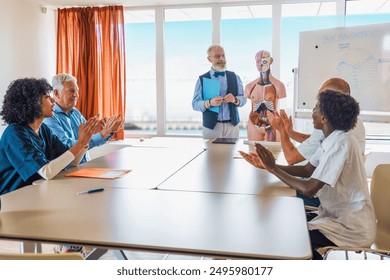 Senior professor teaching anatomy to diverse group of medical students using anatomical model. Multicultural class applauding during educational presentation - medical education and lifelong learning. - Powered by Shutterstock