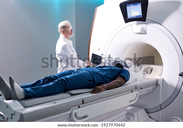 Senior Radiologist Controls\
MRI or CT or PET Scan with Male Patient Undergoing Procedure.\
High-Tech Modern Medical Equipment. Friendly Doctor Working With\
Patient