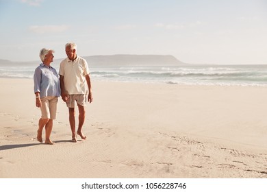 Senior Retired Couple Walking Along Beach Hand In Hand Together - Powered by Shutterstock