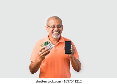Senior retired Old Indian asian man showing medicine blistep pack of tablets with currency or mobile screen - online order concept