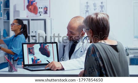 Senior retired woman patient in visit to her cardiologist doctor. Heart disease problems presented by cardiologist cardiology, heart attach. Health care in modern private clinic. Medical staff