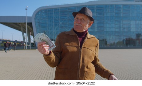 Senior Rich Pensioner Tourist Grandfather Businessman Stay Near International Airport Hall Or Railway Station Holding Cash Money In Dollar Banknotes Celebrate Success Win. Travel, Vacation, Holidays