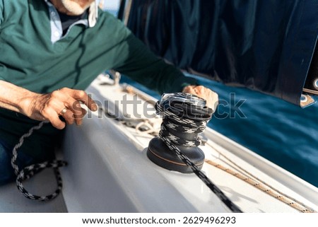 Senior sailor operating a winch to adjust sails during a maritime journey, enjoying the thrill of sailing on the open sea