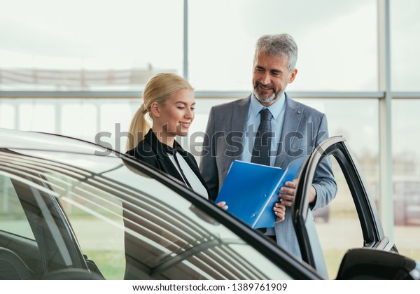 senior sales agent showing car brochure to\
customer in car dealers\
showroom