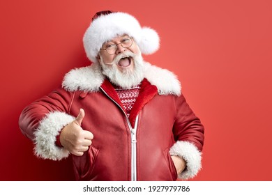 senior santa in red coat and hat shows thumbs up isolated over red studio background, handsome happy man ready to please people, happy with the result