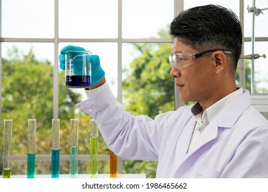 Senior scientist with safety goggle holding and looking blue solvent liquid beaker during research in laboratory - Powered by Shutterstock