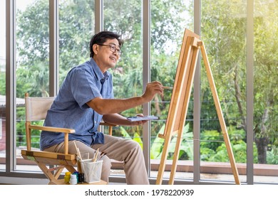 Senior smiling Asian man using brush and water color to paint on canvas. Happy retirement and activity concept. - Powered by Shutterstock