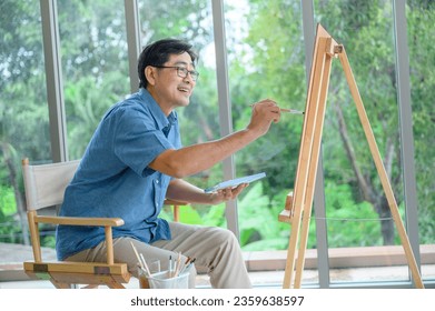 Senior smiling Asian man using brush and water color to paint on canvas. Happy retirement and activity concept. - Powered by Shutterstock