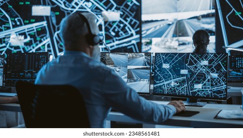 Senior Specialist in a Dark High-Tech Monitoring Room, Concentrated on a Call and Computer Work. Fleet Manager Using Headphones with Built-In Mic for Communication with Delivery Vehicles - Powered by Shutterstock