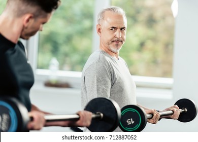 Senior Sportsman Training With Barbells And Young Trainer In Gym    