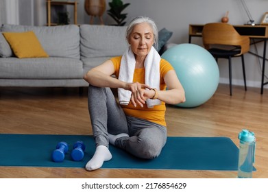 Senior sportswoman using smartwatch fitness tracker after domestic workout, checking burned calories, sitting on floor yoga mat in living room interior - Powered by Shutterstock