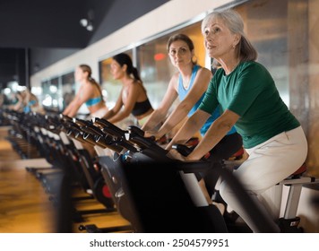 Senior sporty woman doing cardio workout out in female group, training on exercise bike - Powered by Shutterstock