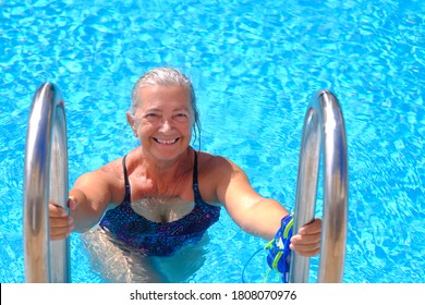 Senior Sporty Woman Smiling Out Of The Pool With Swimming Goggles And Cap In Hand - Active Retiree Enjoying Swimming On A Sunny Day