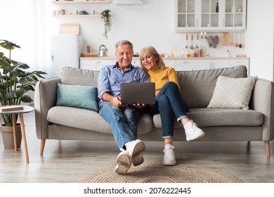 Senior Spouses Using Laptop Watching Movie Together Sitting On Couch At Home. Older Couple Browsing Internet On Computer Reading Online News On Weekend. Technology And Gadgets