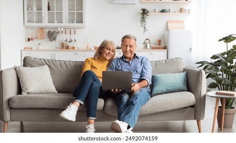 Senior Spouses Using Laptop Watching Movie Together Sitting On Couch At Home. Older Couple Browsing Internet On Computer Reading Online News On Weekend. Technology And Gadgets - Powered by Shutterstock