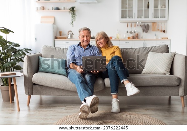 Senior Spouses\
Using Laptop Watching Movie Together Sitting On Couch At Home.\
Older Couple Browsing Internet On Computer Reading Online News On\
Weekend. Technology And\
Gadgets